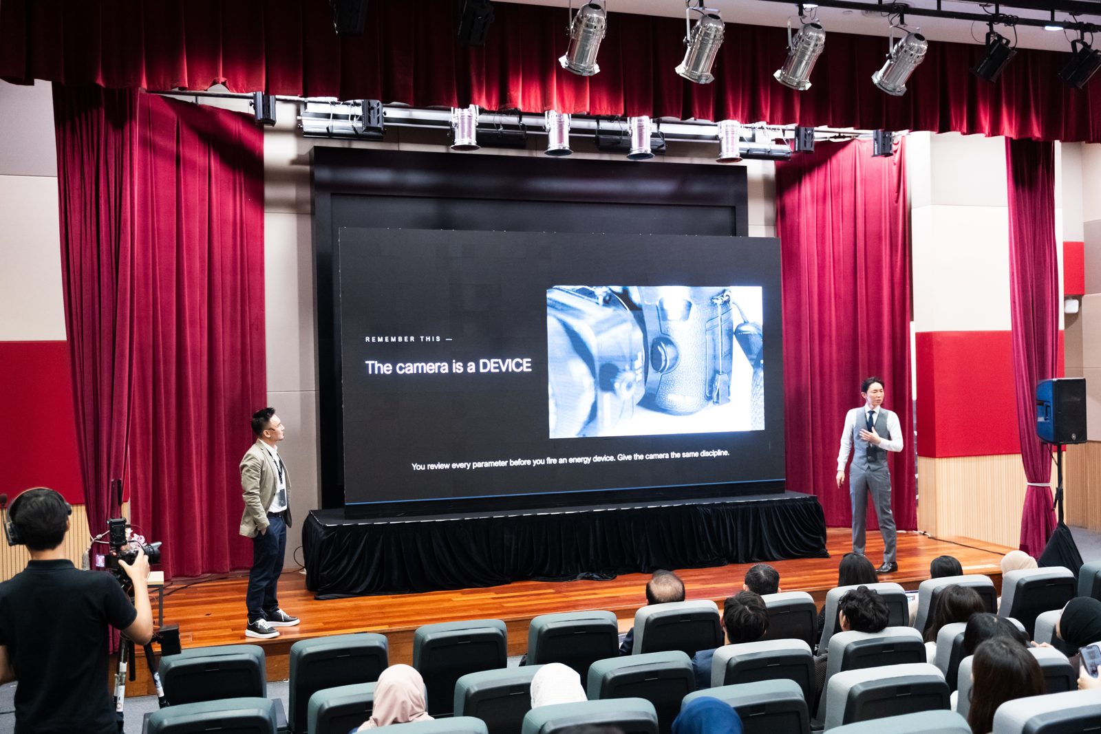 「The camera is a DEVICE」のスライドを挟んで舞台に立つDr. Shangli Linと奥謙太郎院長