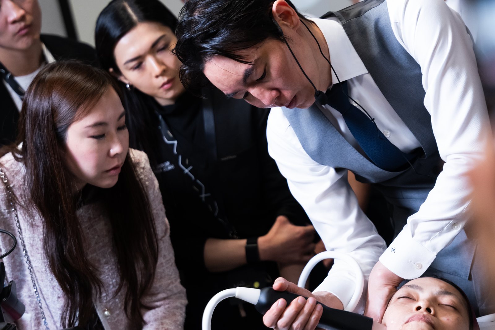 横たわるモデルにハンドピースを当てる奥謙太郎院長と、見つめる参加医師たち